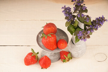 Strawberries and a vase with flowers on a wooden table. A wonderful summer picture of flowers and fresh berries
