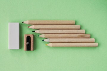 Colored pencils, wooden manual sharpener and eraser on green background. Back to school concept. Set of writing tools for education, creativity, drawing, hobby, art. Eco-friendly stationery