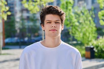 Headshot portrait of handsome guy 19, 20 years old, looking at camera outdoors