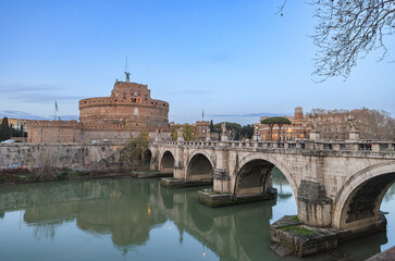 Obraz premium A grand bridge stretches across a tranquil river, leading to a majestic castle nestled in the background. The bridges intricate architecture contrasts against the serene water and lush surroundings