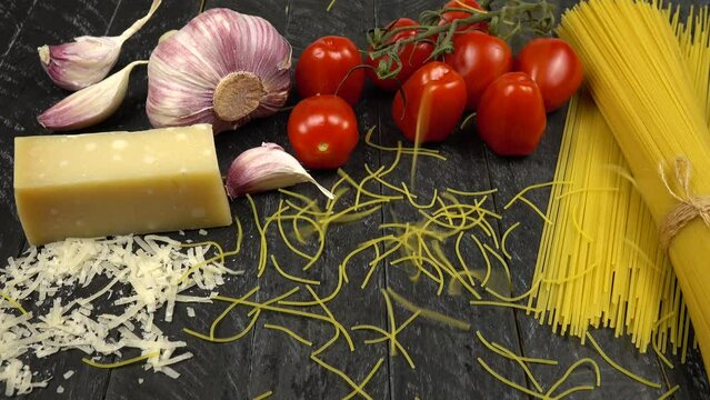 Italian cuisine, traditional pasta and ingredients for it.  Cherry tomatoes, garlic, Parmesan cheese, spaghetti. Vermicelli falling on a black cutting board.