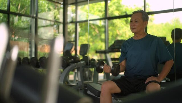 
Senior old man workout weight training biceps muscles with dumbbell in fitness indoor gym. Grandfather mature weight training exercise wearing sportswear. Healthy Aging Society concept.