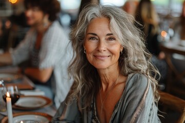 An image of an attractive senior lady with silver hair, smiling softly at a restaurant table