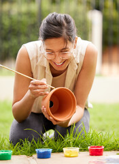 Clay, pot and girl painting a craft container for plant in garden with creativity in hobby. Ceramic, art and happy artist outdoor with paint brush for fun decoration project for house and gardening © peopleimages.com