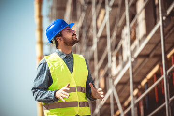 Construction site manager standing  wearing safety vest and helmet, thinking at construction site. Young architect watching construction site with confidence.
