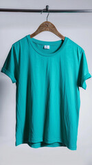 A bright teal t-shirt suspended from a carved mahogany hanger, set before a pure white backdrop. 