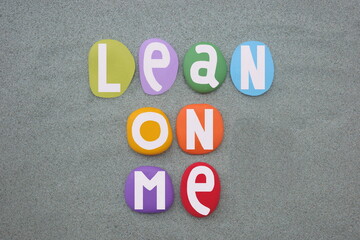 Lean on me, motivational slogan composed with hand painted multi colored stone letters over green...