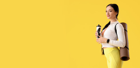Portrait of sporty young woman with water bottle and yoga mat on yellow background
