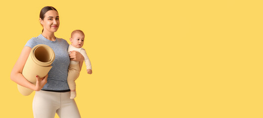 Beautiful young sporty woman with yoga mat holding her little baby on yellow background