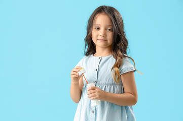 Cute little girl blowing soap bubbles on light blue background