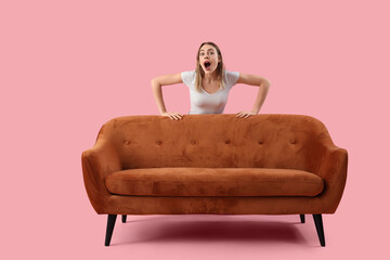 Surprised young woman behind sofa on pink background