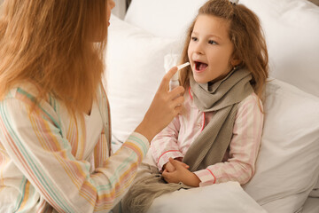 Sick little girl with her mother spraying sore throat in bedroom