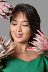 Young Asian woman with beautiful protea flowers on grey background, closeup