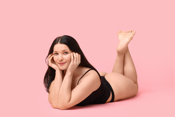 Body positive young woman in underwear lying on pink background