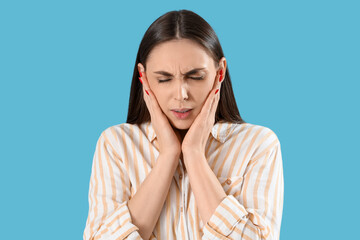 Young woman suffering from toothache on blue background, closeup