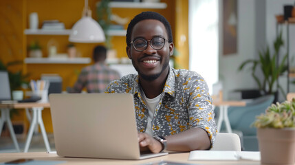 Portrait of smiling African American man in glasses sit at desk in office working on laptop, happy biracial male worker look at camera posing, busy using modern computer gadget at workplace - Powered by Adobe
