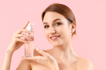 Beautiful young woman with bottle of cosmetic product on pink background