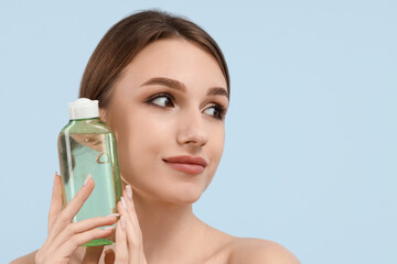 Beautiful young woman with bottle of micellar water on blue background