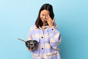 Young brunette mixed race woman holding a bowl full of noodles over isolated blue background with...
