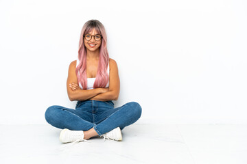 Young mixed race woman with pink hair sitting on the floor isolated on white background keeping the...