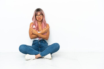 Young mixed race woman with pink hair sitting on the floor isolated on white background pointing to...