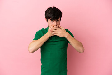 Young Russian man isolated on pink background covering mouth with hands