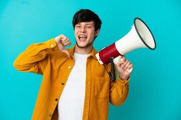 Young Russian man isolated on blue background holding a megaphone and proud and self-satisfied