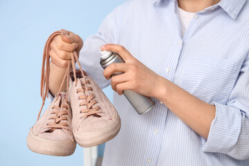 Woman applying water repellent spray over pair of gumshoes on color background, closeup