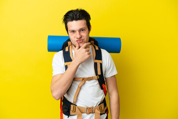 Young mountaineer Russian man with a big backpack isolated on yellow background thinking