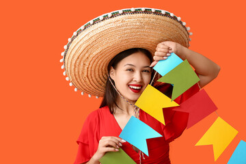 Happy young woman in Mexican sombrero hat and with garland on orange background