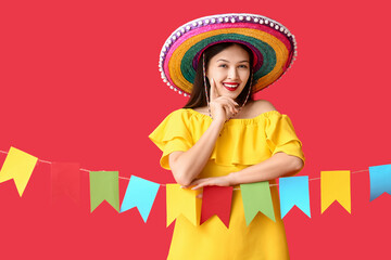 Happy young woman in Mexican sombrero hat and with garland on red background