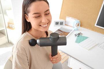 Young woman massaging her shoulder with percussive massager at home office. closeup