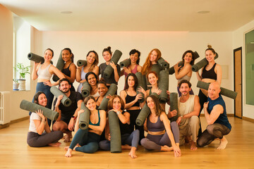 A large group of people are posing for a photo with yoga mats. Scene is positive and energetic, as everyone is smiling and holding their mats. The idea of the image is to capture a moment of camarader