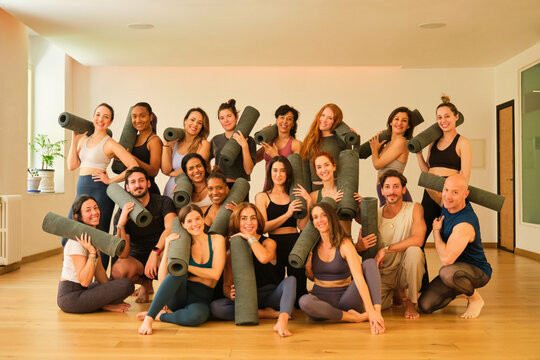 A large group of people are posing for a photo with yoga mats. Scene is positive and energetic, as everyone is smiling and holding their mats. The idea of the image is to capture a moment of camarader