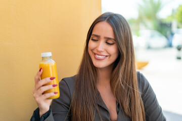 Young woman holding an orange juice at outdoors with happy expression
