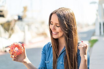 Young woman holding a donut at outdoors celebrating a victory