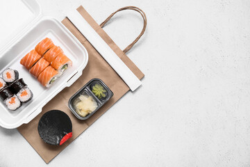 Plastic container with tasty sushi rolls, soy sauce and paper bag on white grunge background. Delivery concept