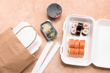 Plastic container with tasty sushi rolls, soy sauce and paper bag on beige grunge background....