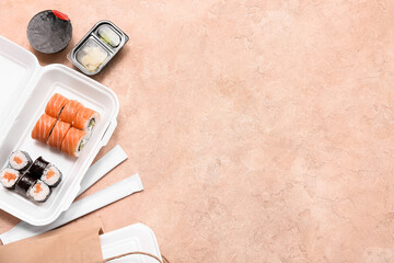 Plastic container with tasty sushi rolls, soy sauce and chopsticks on beige grunge background. Delivery concept