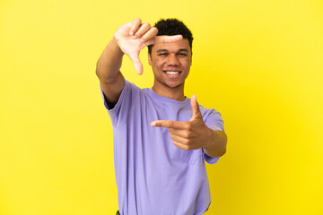 Young African American man isolated on yellow background focusing face. Framing symbol