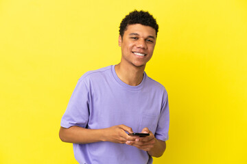 Young African American man isolated on yellow background sending a message with the mobile