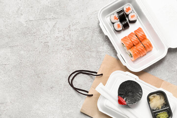 Plastic containers with tasty sushi rolls, soy sauce and paper bag on grey grunge background....