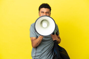 Young sport African American man with sport bag isolated on yellow background shouting through a...