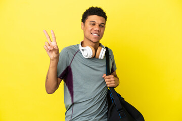 Fototapeta premium Young sport African American man with sport bag isolated on yellow background smiling and showing victory sign