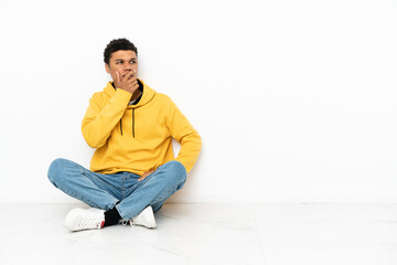 Young African American man sitting on the floor isolated on white background having doubts and with...