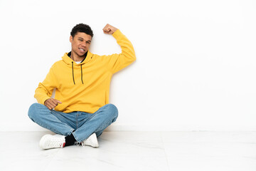 Young African American man sitting on the floor isolated on white background doing strong gesture