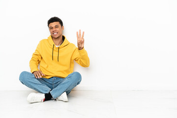 Young African American man sitting on the floor isolated on white background happy and counting...