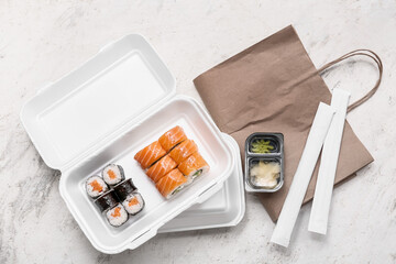 Plastic containers with tasty sushi rolls, chopsticks and paper bag on white grunge background. Delivery concept