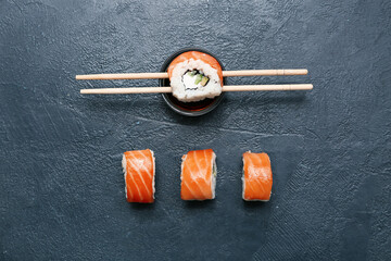 Tasty sushi rolls with chopsticks and soy sauce on black grunge background