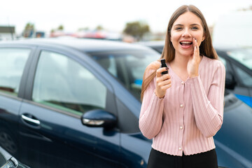 Young pretty blonde woman holding car keys at outdoors shouting with mouth wide open